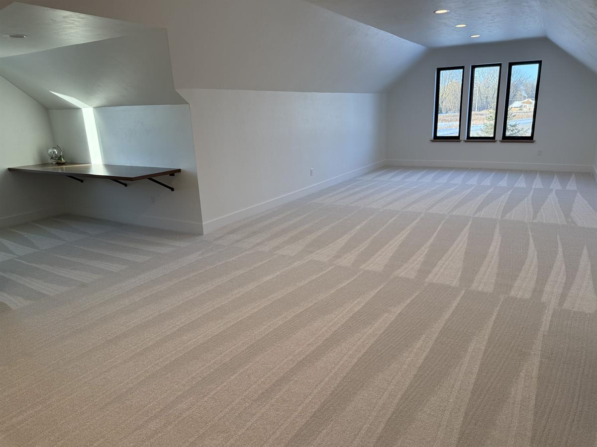Bonus room with vaulted ceiling, built-in desk nook, and freshly cleaned cream carpet