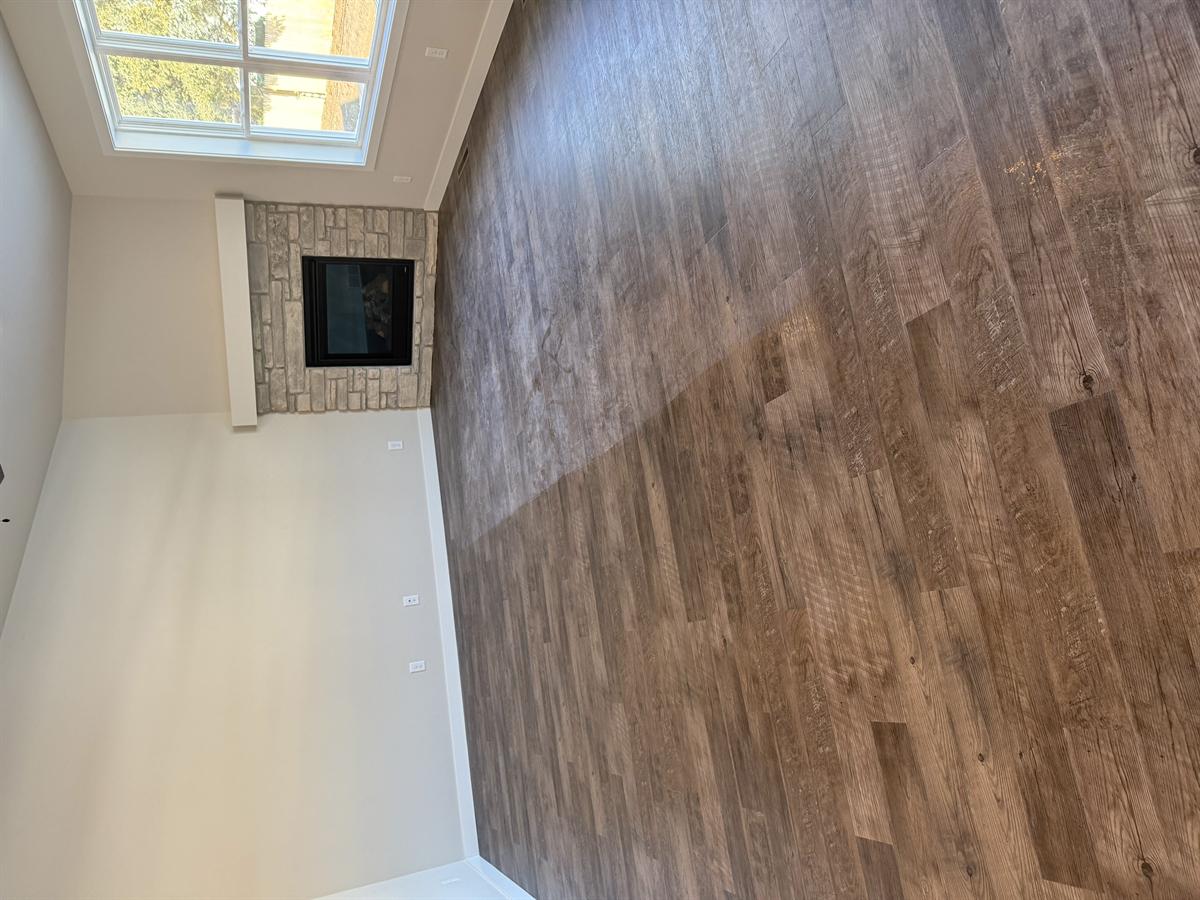 Living room floor covered in construction dust — stone corner fireplace and large window