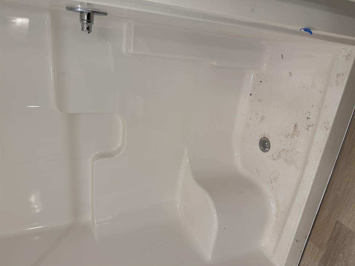Walk-in shower stall with construction dirt and debris in the basin before cleaning