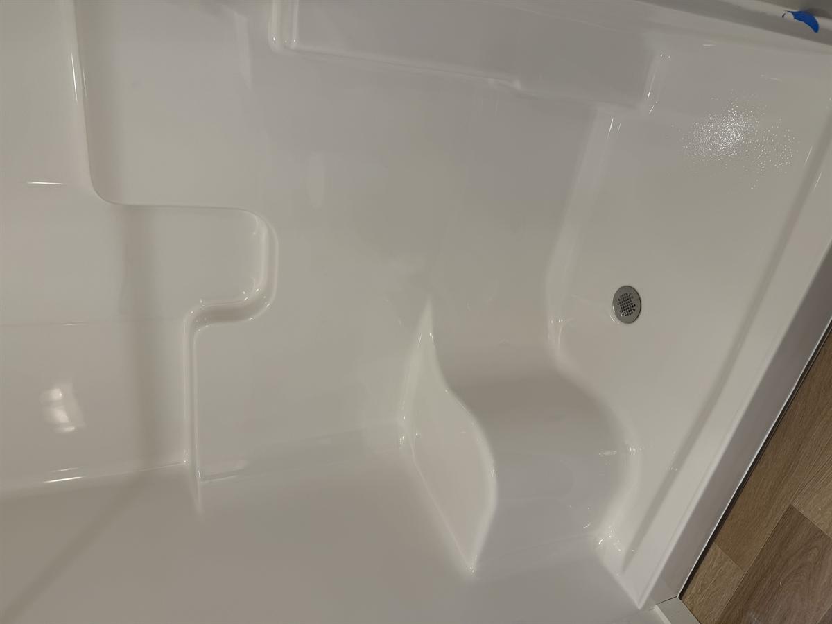 Walk-in shower stall with built-in bench, sparkling clean white fiberglass after construction clean