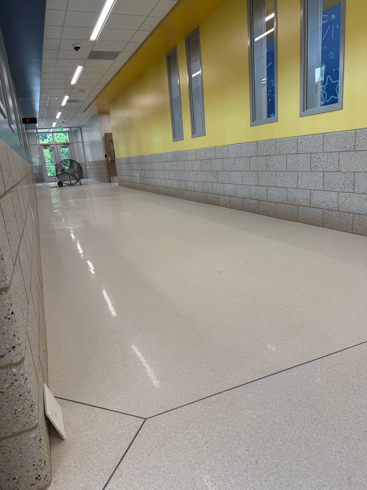 School hallway with polished terrazzo floor, yellow walls, and speckled block wainscot after cleaning