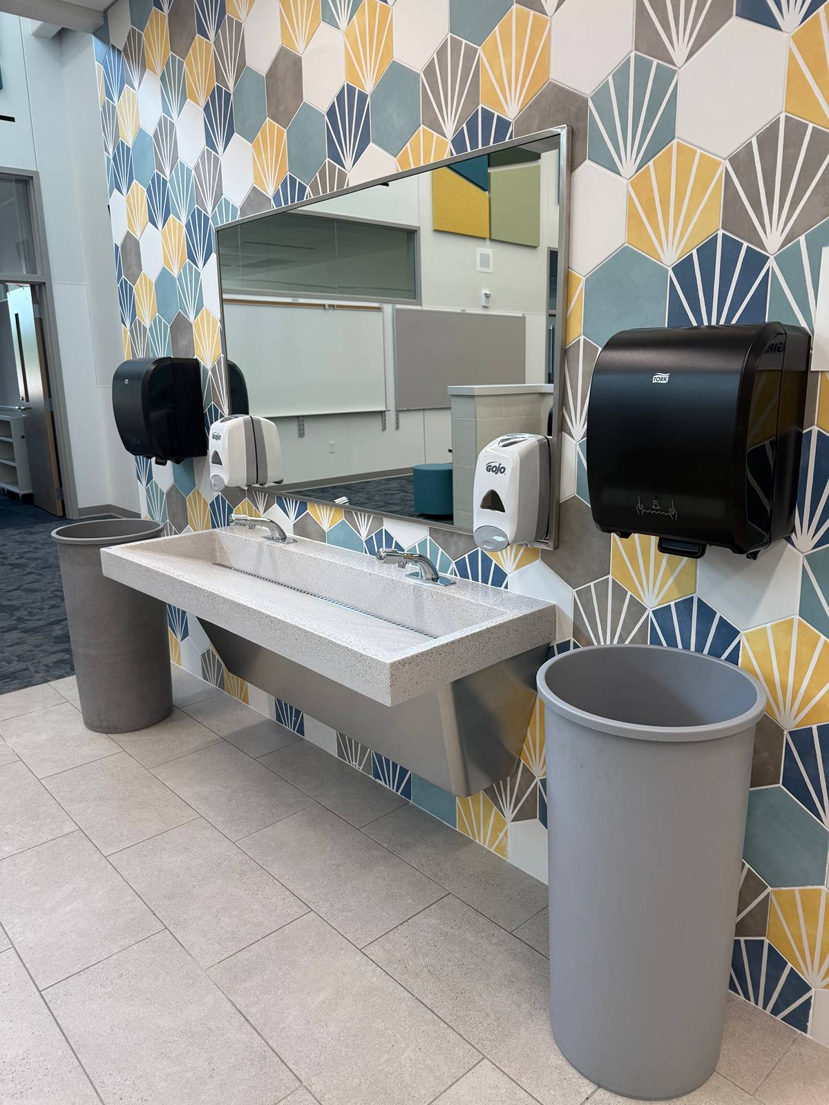 Trough sink and mirror against a hexagon tile wall, with clean tile floor